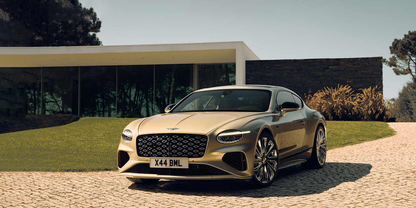 Bentley Essex (Chelmsford) Bentley Continental GT Mulliner coupe front three quarters in Patina paint parked outside a glass fronted building with a grass lawn behind it