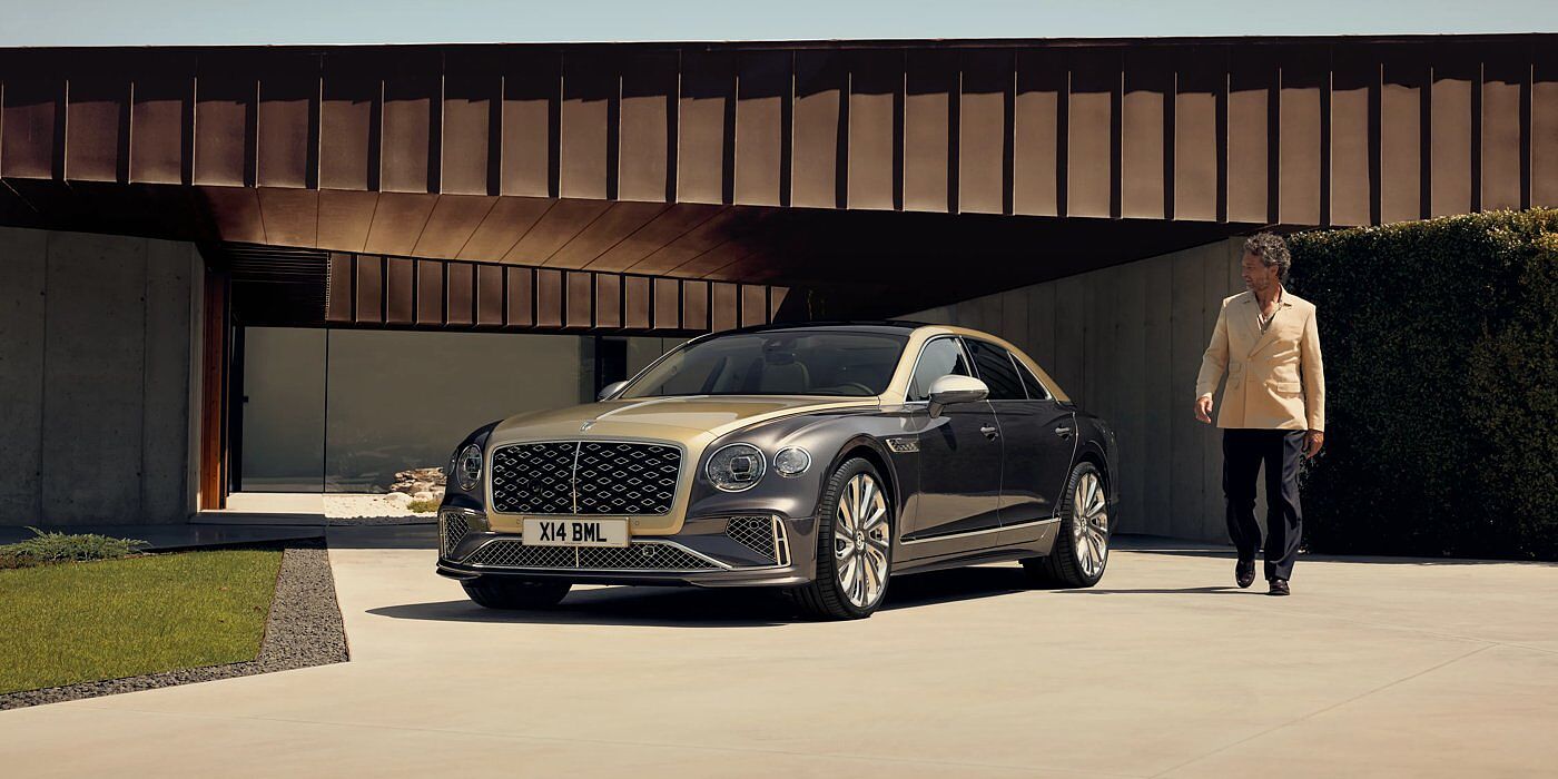 Bentley Essex (Chelmsford) Bentley New Flying Spur Mulliner V8 hybrid sedan front three quarters in Rose Gold over Magnetic paint, parked near modern home