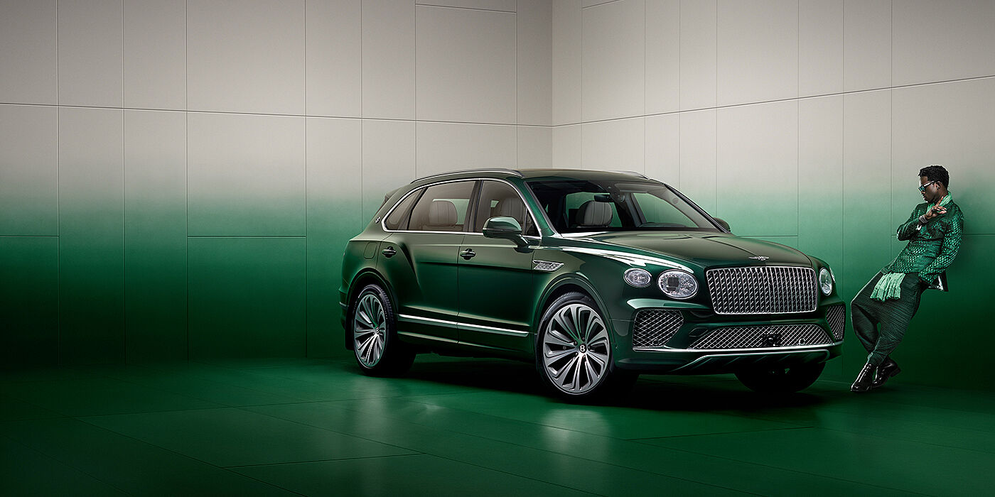 Bentley Essex (Chelmsford) Wisdom K leans against wall next to Bentley Bentayga Extended Wheelbase Atelier Edition SUV in Light Emerald green paint