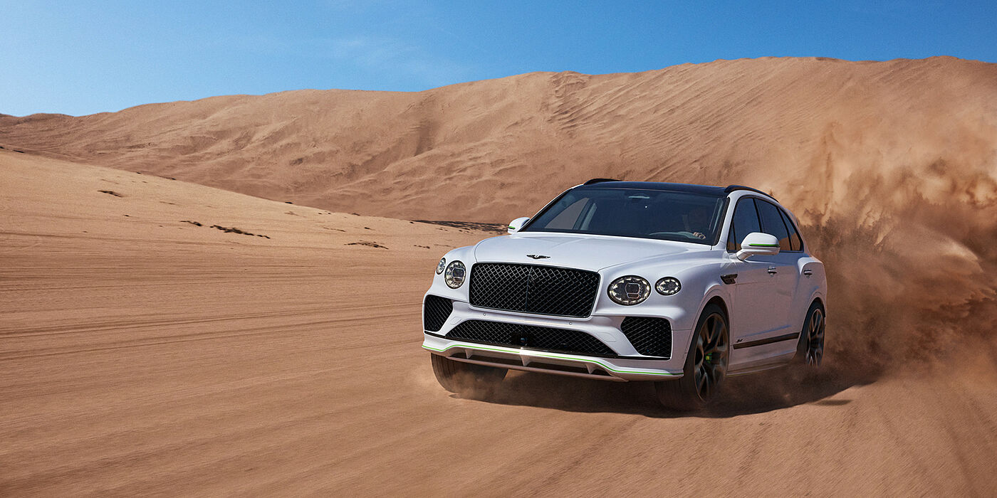 Bentley Essex (Chelmsford) Bentley Bentayga Speed SUV front three quarter in Snow Quarts Pearlescent by Mulliner white paint driving dynamically through the desert