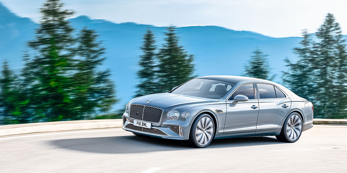 Bentley Essex (Chelmsford) New Bentley Flying Spur sedan side view in Silverlake paint with ten spoke wheels and chrome matrix grille driving dynamically on a mountain road