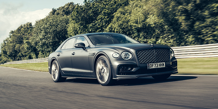 Bentley Essex (Chelmsford) Bentley Flying Spur Mulliner sedan front three quarter in dark grey paint driving dynamically by some trees on a track