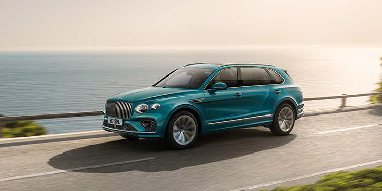 Bentley Essex (Chelmsford) Bentley Bentayga Extended Wheelbase Azure SUV in Topaz blue paint driving dynamically by the ocean