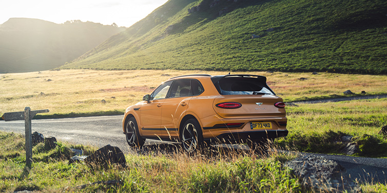 Bentley Essex (Chelmsford) Bentley Bentayga S SUV rear three quarter in Sunburst Gold paint on a road surrounded by green hills