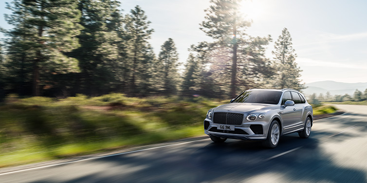 Bentley Essex (Chelmsford) Bentley Bentayga SUV front three quarter in Moonbeam silver paint driving dynamically along a tree-lined road