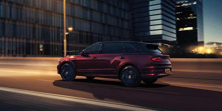 Bentley Essex (Chelmsford) Bentley Bentayga Extended Wheelbase Mulliner SUV in Cricket Ball red paint driving dynamically in city at night