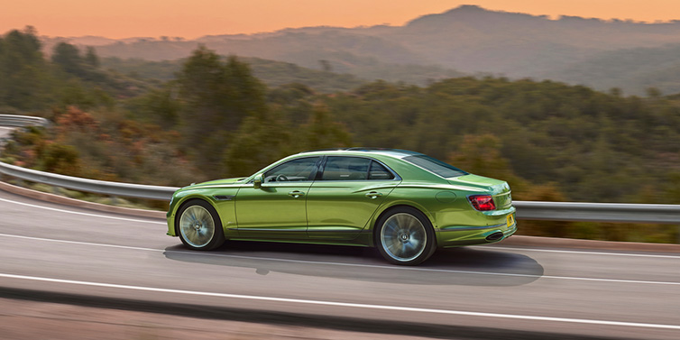 Bentley Essex (Chelmsford) Bentley Flying Spur Speed sedan side profile in Tourmaline Green paint driving dynamically on a mountain road at sunset