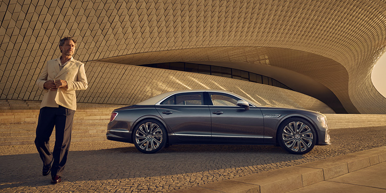 Bentley Essex (Chelmsford) Bentley Flying Spur Mulliner sedan in Rose Gold over Magnetic duotone paint parked by a curved wall with person in suit jacket standing on the left